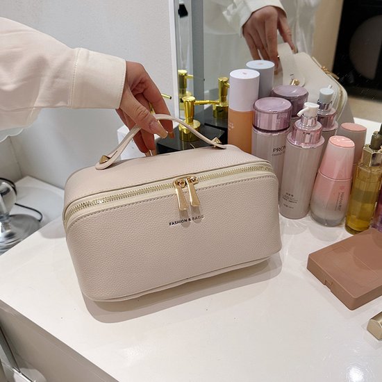 Crèmekleurige toilettas met handvat en gouden rits, naast diverse make-upproducten.
