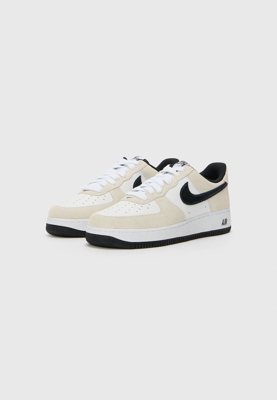 Paar witte sneakers met beige suède overlays, zwart Swoosh-logo en "AIR" op de zool.