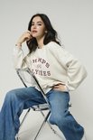 Model op stoel draagt een lichtgrijze sweater met 'CHAMPS Paris ÉLYSÉES' opdruk en een blauwe jeans.