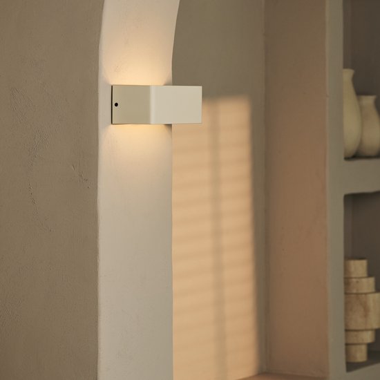 Vanillekleurige wandlamp met opgaande en neerwaartse lichtbundels, gemonteerd op een muur.