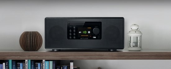 Zwart micro-audiosysteem met display, bedieningsknoppen, CD-speler en luidsprekers, op een plank met decoratie.
