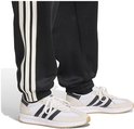 Detail van de broekspijpen van een zwarte trainingsbroek met witte strepen, gedragen met witte sneakers.