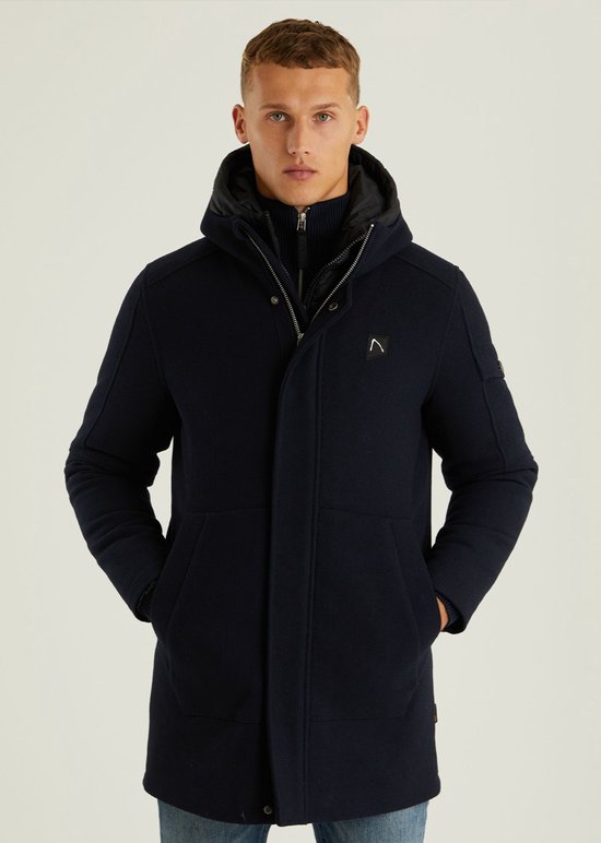 Man met donkerblauwe wollen parka met capuchon en met de handen in de zakken.