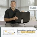 Een man houdt een zwart orthopedisch zitkussen van traagschuim omhoog, met de verpakking.
