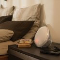 Philips wek-up light op een donker nachtkastje, naast een stapel boeken en een telefoon, de tijd 09:32 wordt getoond.