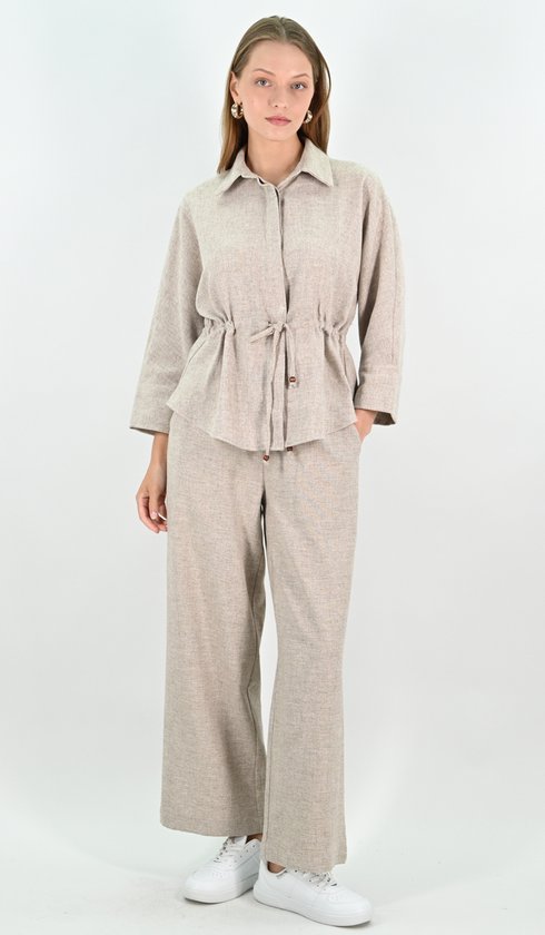 Mannequin porte une tenue couleur naturelle en mélange de lin. La tenue comprend une blouse avec cordon de serrage à la taille et un pantalon large. Baskets blanches.