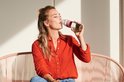 Vrouw in oranje blouse drinkt uit een Mepal waterfles met roze band.