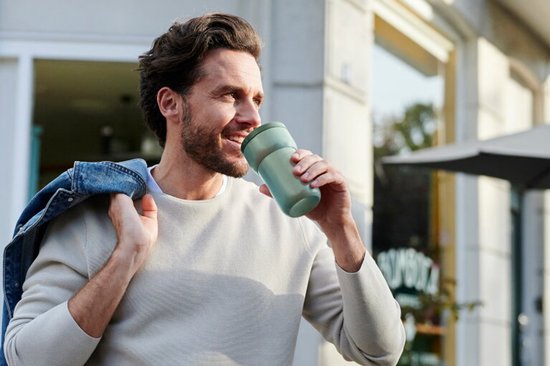 Homme buvant d'une tasse vert clair dans ses mains à l'extérieur.