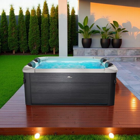 Luxe grijze jacuzzi met 6 zitplaatsen, omgeven door een houten terras en groene tuin.