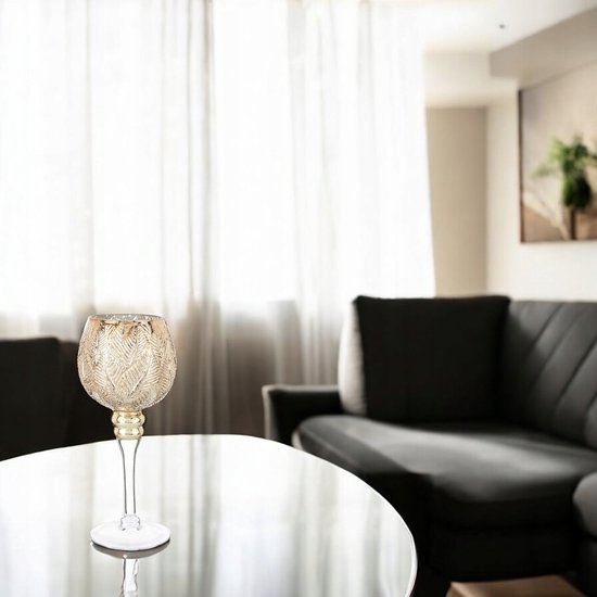 Gouden glazen kandelaar geplaatst op een glazen tafel in een woonkamer met een donkere bank.