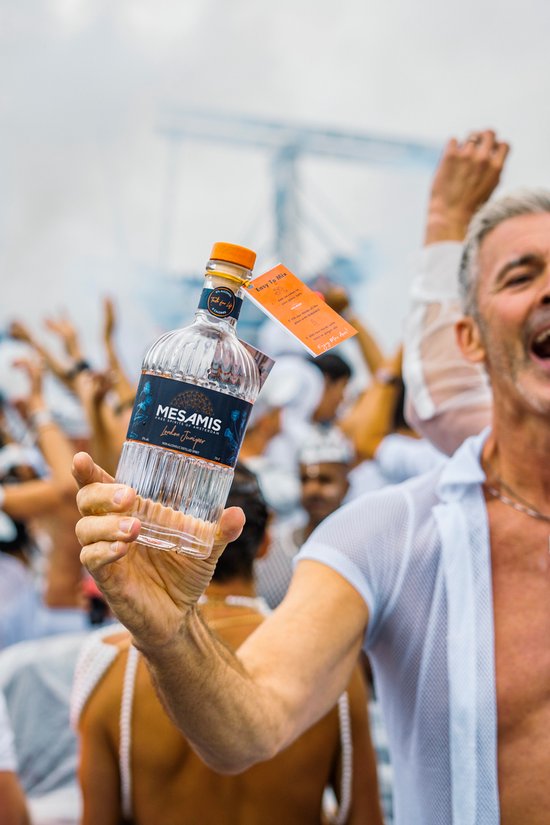 Man met witte kleding houdt een fles Mesamis London Juniper omhoog in een menigte met op de achtergrond rook.