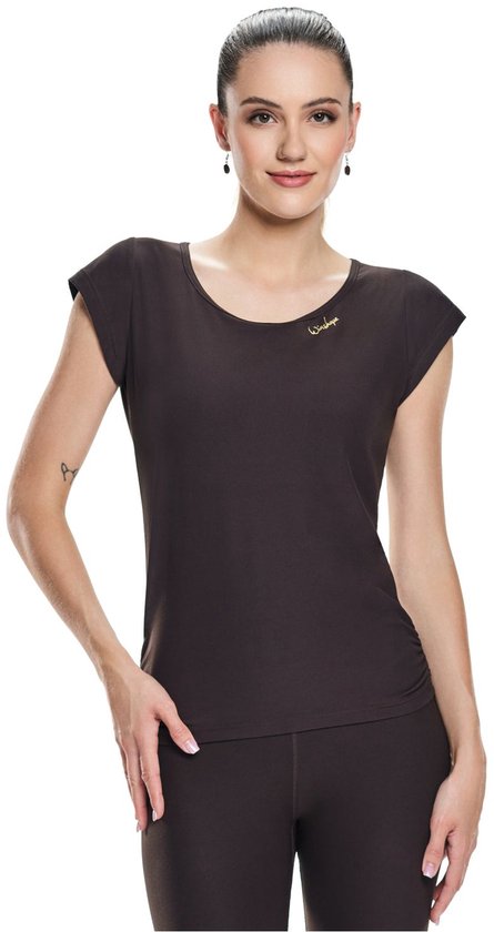 Model draagt een donkerbruin shirt met korte mouwen en ruches aan de zijkanten. Een klein gouden logo is op de borst geborduurd.