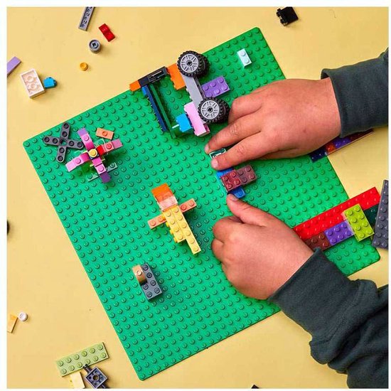 Kinderhanden bouwen met kleurrijke LEGO stenen op groene bouwplaat, met diverse modellen.
