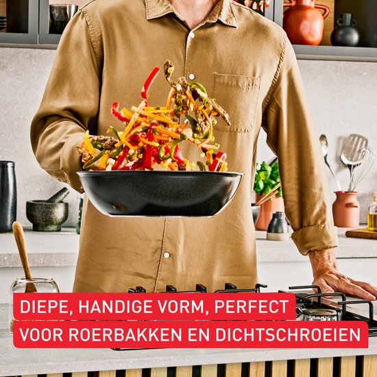 Man in bruin hemd gooit groenten en vlees in een zwarte wokpan. "DIEPE, HANDIGE VORM, PERFECT VOOR ROERBAKKEN EN DICHTSCHROEIEN"