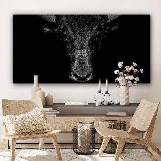 Toile noir et blanc d'un taureau sur fond sombre, au-dessus d'un buffet décoré.