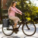 Vrouw met roze blouse op fiets met zwarte Vebics fietstas rugzak.