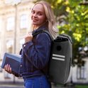 Blonde vrouw met boeken draagt zwarte Vebics fietstas rugzak met reflecterende strepen.