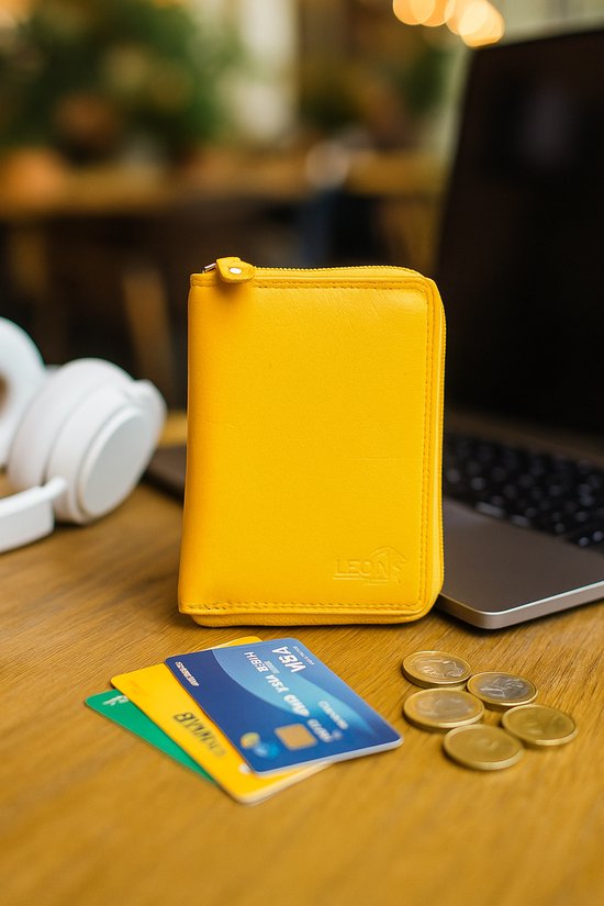 Gele, leren portemonnee op een houten tafel met creditcards, munten en koptelefoon.