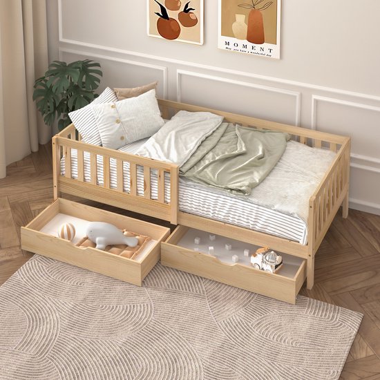Houten peuterbed met spijlen, gestreepte bedlinnen, twee open lades met speelgoed en een bloemenkussen.