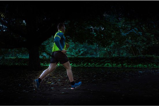 Man joggend in het donker met een fluoriserend geel en blauw sportshirt met reflecterende details.
