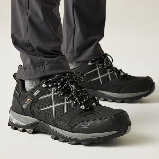 Man met grijze broek en sokken draagt een zwarte wandelschoen met grijze accenten.