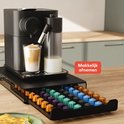 Zwarte capsulehouder met lade vol gekleurde Nespresso cups, geplaatst onder een Nespresso machine.