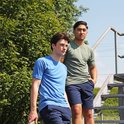 Twee mannen, één in blauw T-shirt en navy short, één in groen T-shirt en navy short, op een trap.