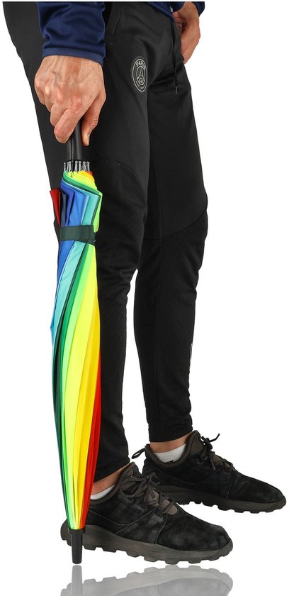Een man met sportbroek houdt een gesloten regenboogparaplu vast. De paraplu is in elkaar gevouwen met veelkleurige vlakken.
