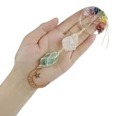 Hand houdt een hanger vast met een levensboom in regenboogkleuren, twee ruwe edelstenen en een gouden maan met ster.