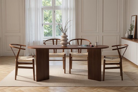 Eettafel van donker hout met een ovaal blad, geflankeerd door stoelen met gebogen rugleuningen en gevlochten zittingen.