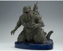 Grijze Godzilla figuur met scherpe rugplaten, knielend op een blauwe waterbasis met logo.