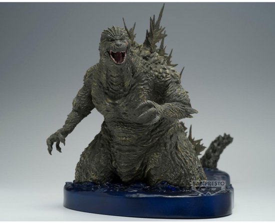 Grijze Godzilla figuur met scherpe rugplaten, knielend op een blauwe waterbasis met logo.