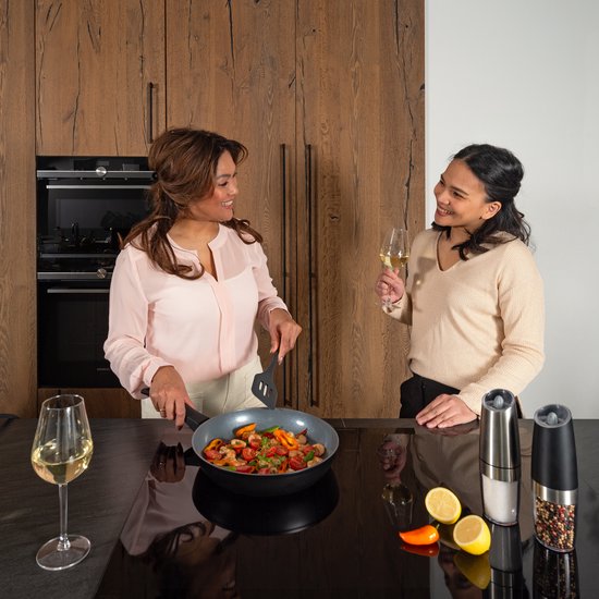 Twee vrouwen koken samen in een keuken, één bakt een ei, de ander groenten.