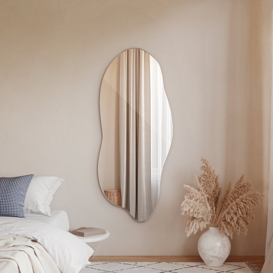 Miroir asymétrique de forme organique sur un mur dans une chambre avec lit et plantes.
