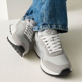 Grijze lage sneakers met witte veters en blauwe jeans, van bovenaf gezien.