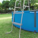 Grijze ladder naast een ronde blauwe zwembad.