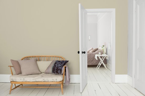 Lichte groene muur in een woonkamer met bankje en open deur naar een slaapkamer.