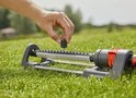 Een hand plaatst een zwart opzetstuk op een Gardena zwenksproeier.