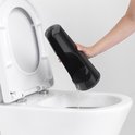 Main tenant le support de brosse à toilettes noir vide au-dessus d'une toilette.