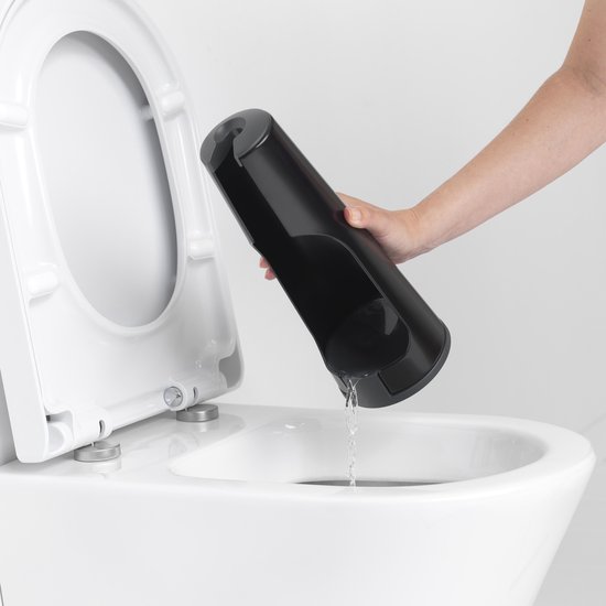 Main tenant le support de brosse à toilettes noir vide au-dessus d'une toilette.