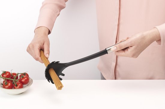 Handen houden een spaghettilepel met ongekookte spaghetti vast, naast een kom tomaten.