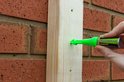 Een hand gebruikt een groene Marxman pen om een markering op een houten balk te maken.