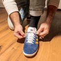 Een persoon die een blauwe schoen met gele strepen strikt. Een zwarte sok is zichtbaar.