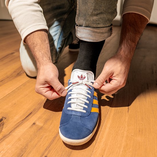 Een persoon die een blauwe schoen met gele strepen strikt. Een zwarte sok is zichtbaar.