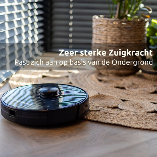 Zwarte robotstofzuiger staat op een jute mat naast een plant in een rieten mand. Tekst: "Zeer sterke Zuigkracht Past zich aan op basis van de Ondergrond".