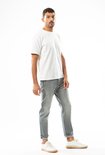 Man in een witte T-shirt en een lichtgrijze jeans met opgerolde pijpen.
