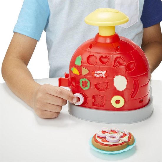 Rode Play-Doh pizzaoven met vormen aan de zijkant, een kind speelt met het apparaat en een nep-pizza ligt ernaast.
