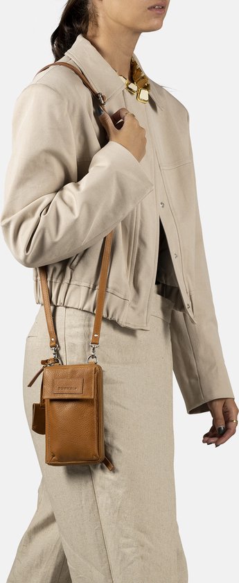 Model met cognac telefoonportemonnee gedragen als crossbody tas, met beige jas en broek.