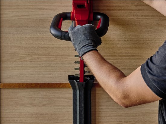 Een hand met handschoen die de Einhell heggenschaar in een zwarte beschermhoes plaatst.