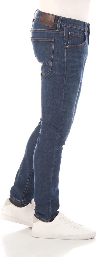 Zijaanzicht van een man in een donkerblauwe jeans met oranje stiksels en een bruin Lee-label.